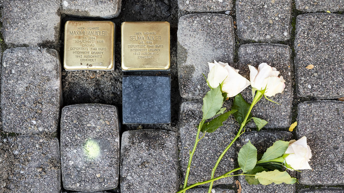 Drei frisch in den Boden verlegte quadratischen Gedenktafeln aus Messing in Speyer und drei weißen Rosen.