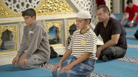 Zwei muslimischer Jungen und ein Erwachsener beten in einer Moschee mit geschlossenen Augen.