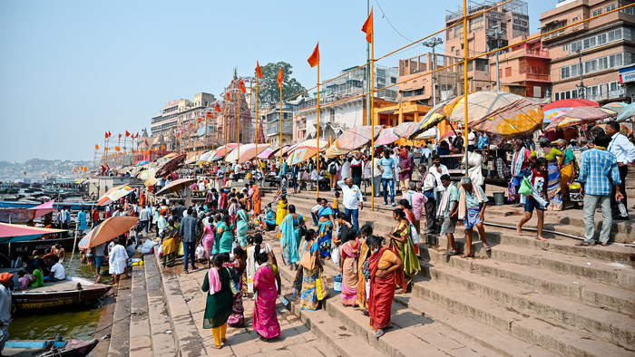 Blick vom Fluß Ganges auf die indische Stadt Benares mit vielen bunten Schiffen und Häusern.