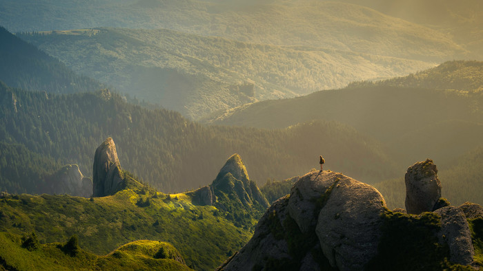 Person steht auf Berg in weitläufiger hügeliger Landschaft