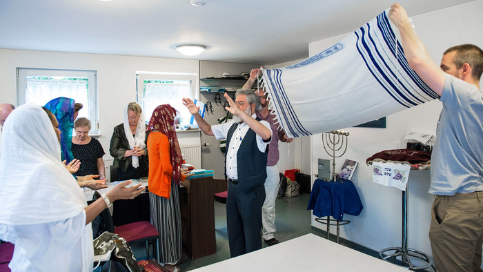 Juden feiern am Freitagabend in einem Raum in Frankfurt am Main Schabbat, wobei die Gemeindemitglieder einen Gebetsschal über den Vorbeter halten.