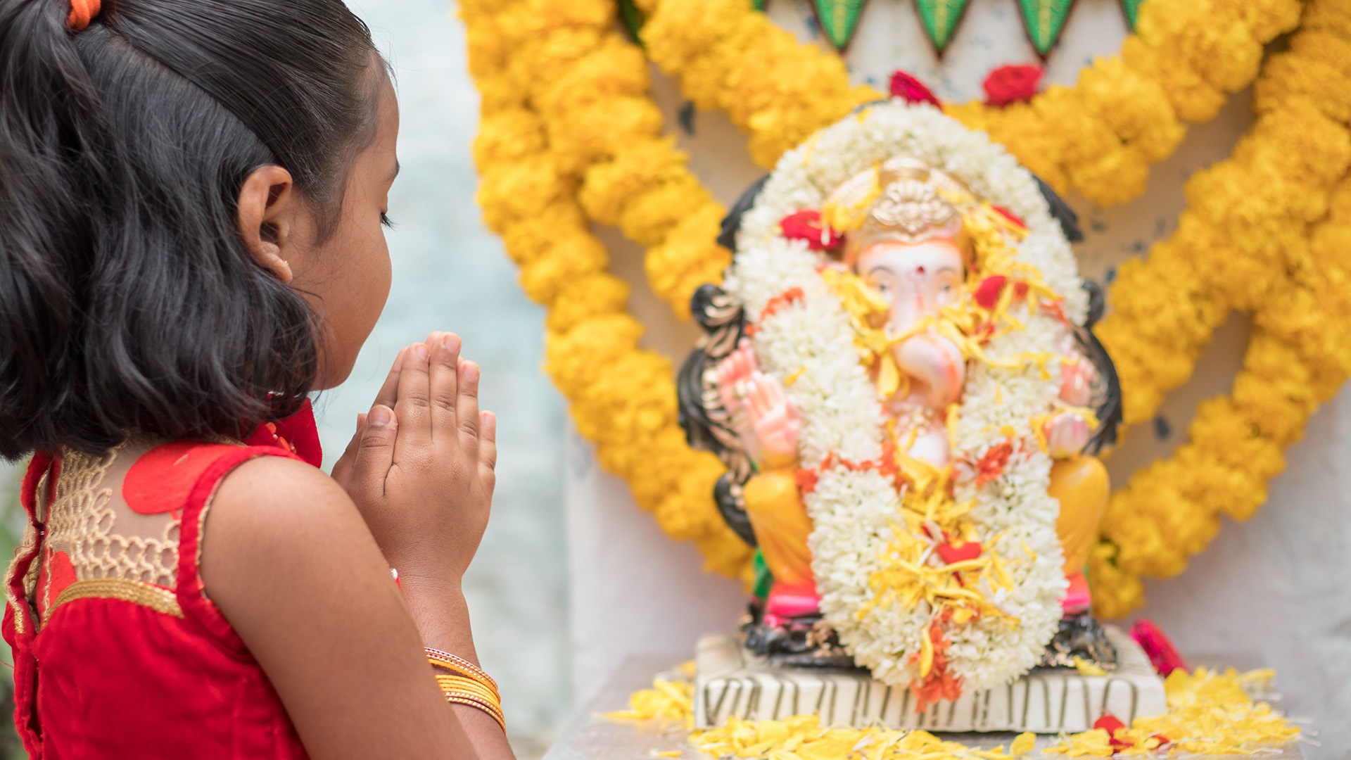 Kind betet mit geschlossenen Augen vor einer Statue von Ganesha