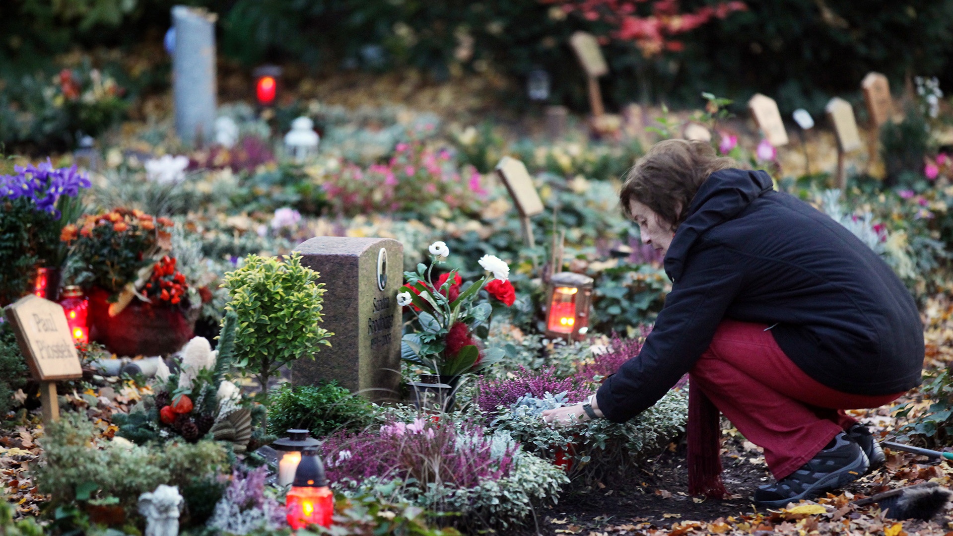 Frau stellt Kerze an Grab an Allerheiligen auf dem Südwestfriedhof in Dortmund