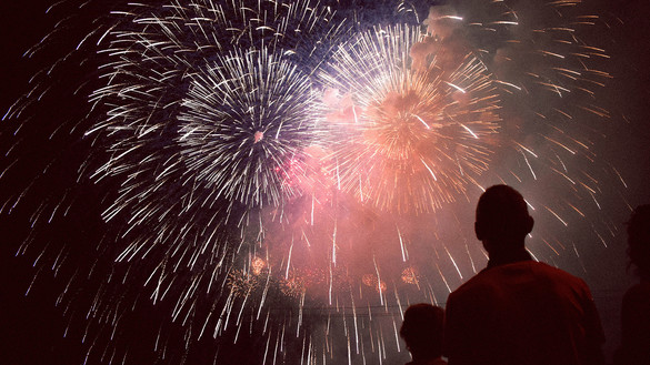 Erwachsener und Kind schauen sich Feuerwerk am Nachthimmel an.