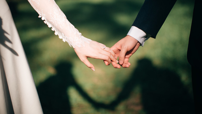 Eine Frau und ein Mann in Hochzeitskleidung halten Händchen.