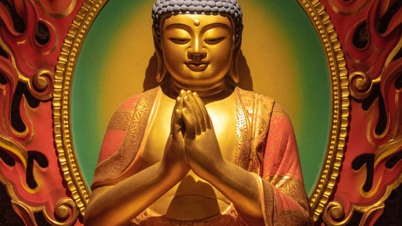 Die Hände einer goldenen Budhhastatue sind zum Gruß zusammengelegt.