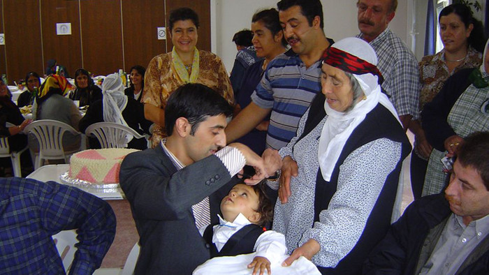 Mann befeuchtet Kopf eines Kindes bei der Taufe