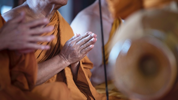 Ein buddhistischer Mann in orangefarbenen Gewand mit zu einer Begrüßung zusammengeführten Handflächen.