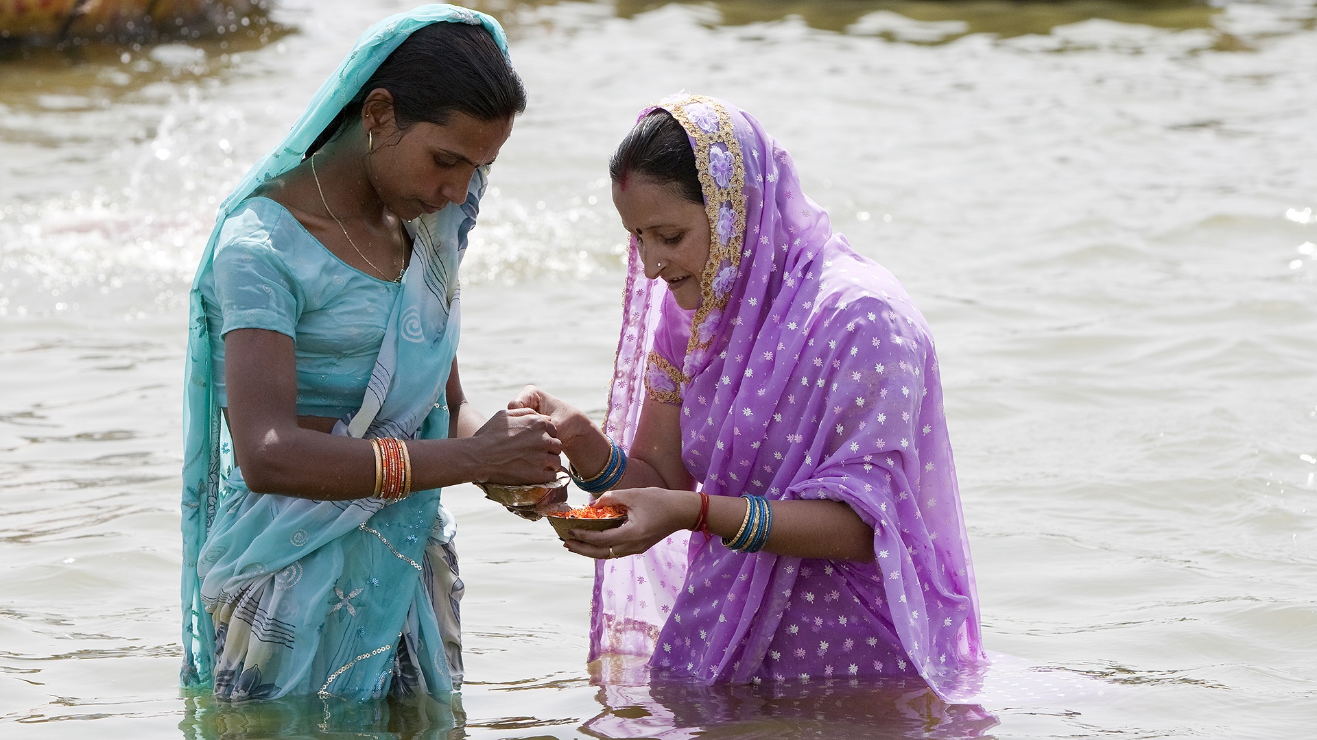 Zwei Frauen legen Blumen und Kerzen im Ganges aus