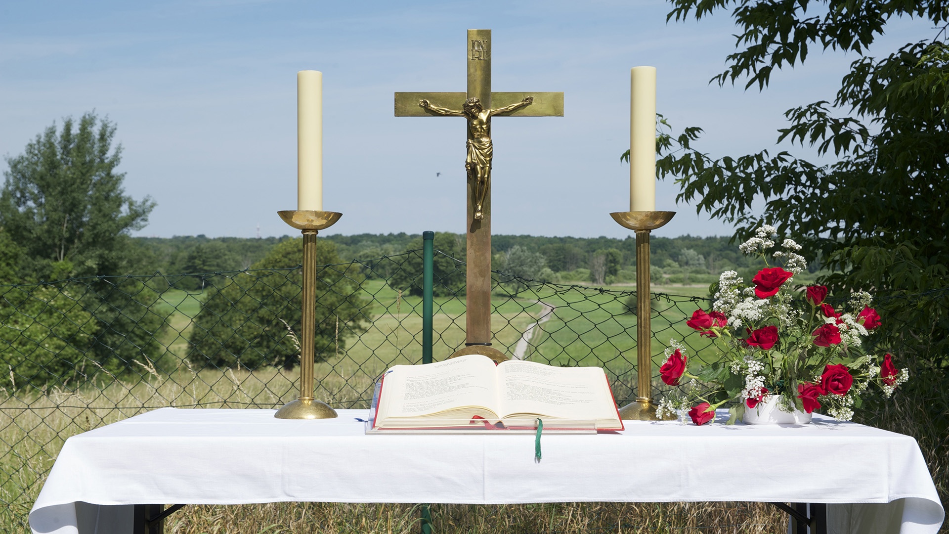 geschmückter Altar eines ökumenischen Freiluftgottesdienstes mit Kreuz, Kerzen, Bibel und Blumen