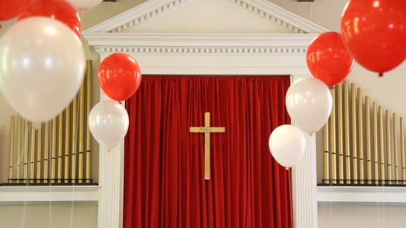 Kreuz umgeben von weißen und roten Luftballons