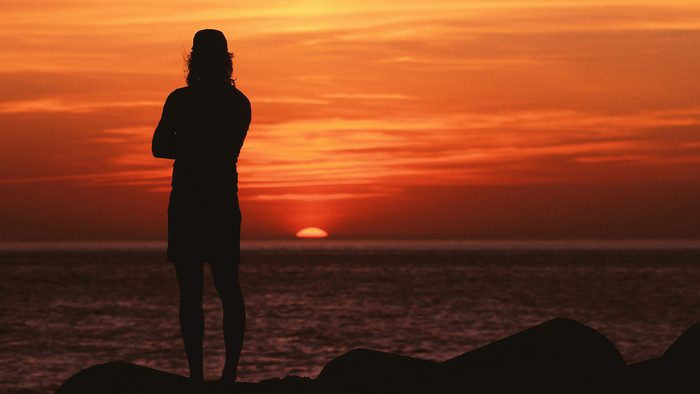 Die Silhouette eines Mannes, der bei Sonnenuntergang auf das Meer blickt.