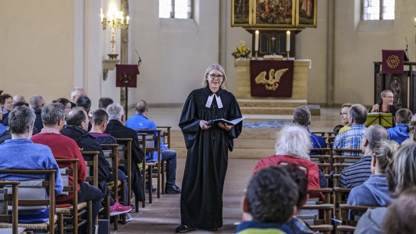 Eine evangelische Pastorin mit Beffchen steht in der Mitte der Kirche, zwischen den sitzenden Gläubigen im Gottesdienst