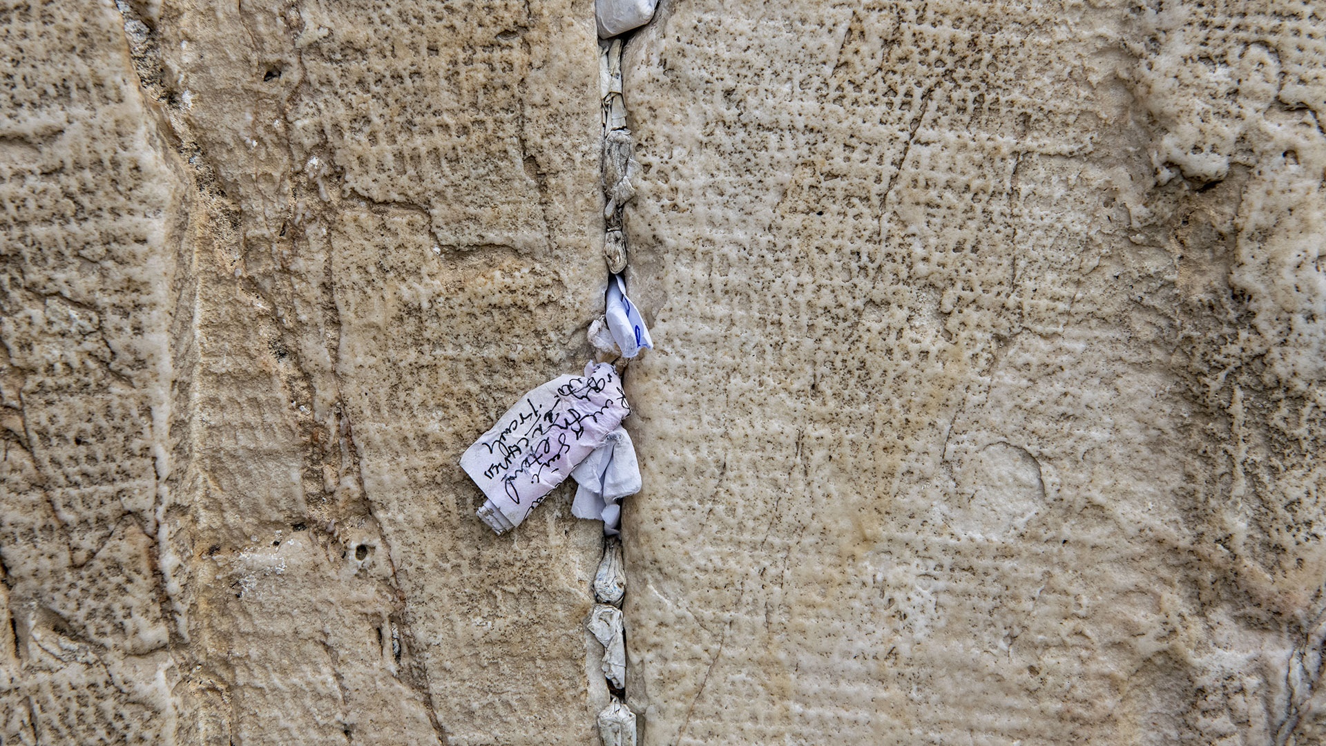 Handgeschriebene Bittzettel in den Ritzen der Mauer