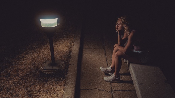 Frau sitzt im Dunkeln vor einer hellen Laterne auf einer Bank.