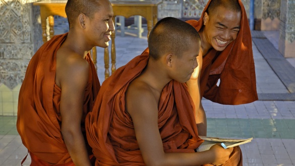 Drei junge buddhistische Mönche aus Myanmar in orangefarbenen Gewändern sitzen auf dem Boden.