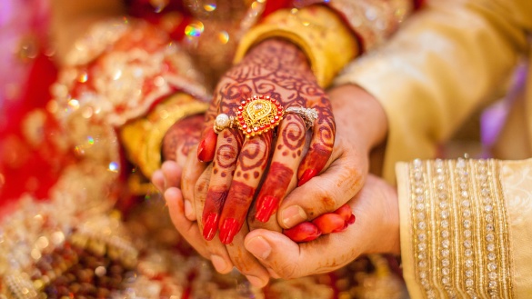 Die mit Henna verzierte und mit Ring geschmückte Hand einer Frau hält die Hand ihres zukünftigen Mannes.