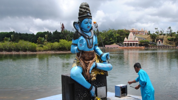 Ein Inder entzündet ein Räucherstäbchen vor einer blauen Statue des Gottes Shiva mit Dreizack.