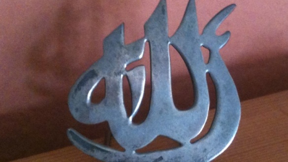 Das arabische Schriftzeichen für Allah aus Metall an einem Holzbrett.