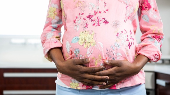 Eine schwangere Frau in einem rosafarbenen T-Shirt umfasst mit beiden Händen ihren Bauch.