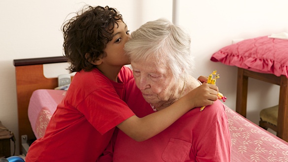 Ein Kind umarmt eine alte Frau, die auf einem Bett sitzt.