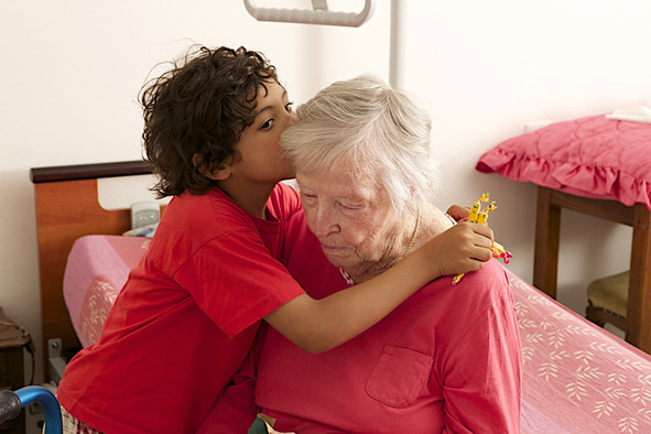Ein Kind umarmt eine alte Frau, die auf einem Bett sitzt.