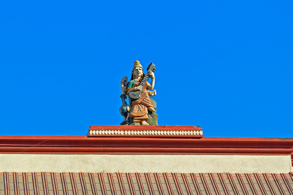 Statue der Hindu-Göttin Sarasvati mit dem Saiteninstrument Vina auf dem Dach eines Tempels