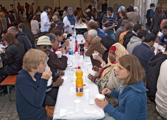 Ein langer Tisch mit Menschen verschiedener Kulturen und Religionen, die sich zum Ende des muslimischen Ramadan zum Essen treffen.