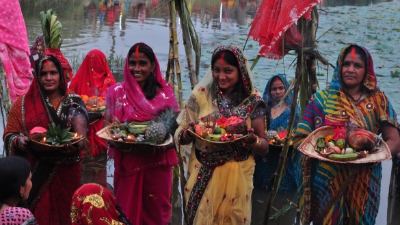 Vier bunt gekleidete Hindufrauen tragen Schalen mit Früchten und Räucherstäbchen.