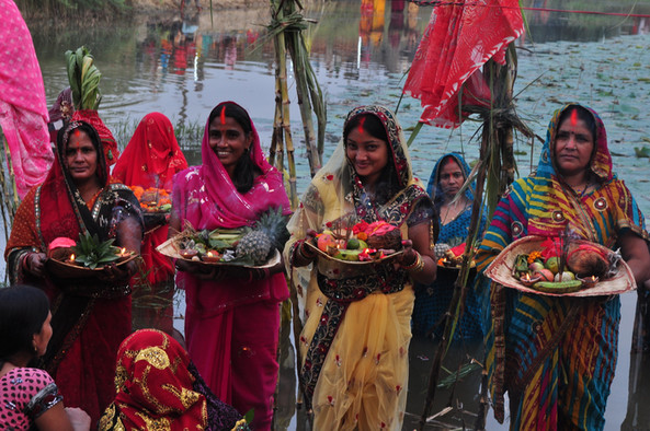 Vier bunt gekleidete Hindufrauen tragen Schalen mit Früchten und Räucherstäbchen.