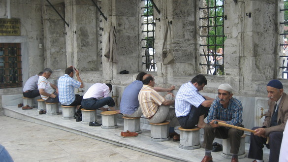 Männer sitzen auf Hockern vor Wasserhähnen einer Moschee und waschen sich.