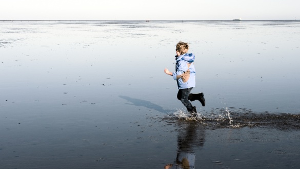 Ein kleiner Junge läuft an einem Strand durch flaches Wasser.