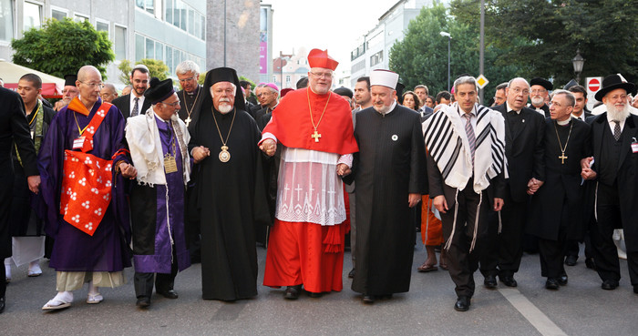 Vertreter verschiedener Weltkirchen gehen bei einem Friedenstreffen in München Hand in Hand.