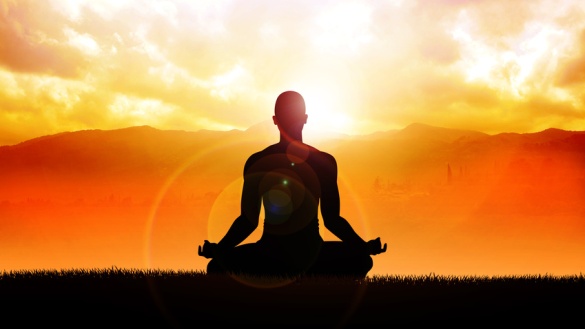Ein meditierender Mensch im Yogasitz vor der aufgehenden Sonne.