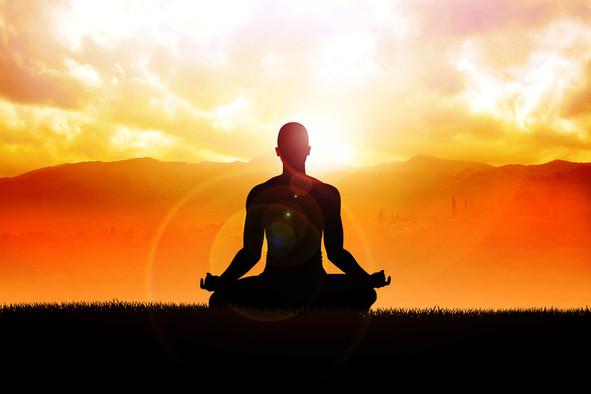 Ein meditierender Mensch im Yogasitz vor der aufgehenden Sonne.