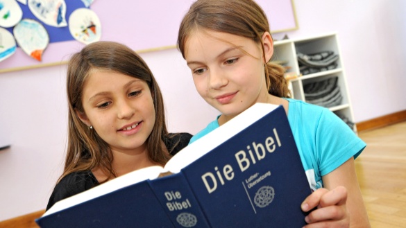 Zwei Mädchen halten eine Bibel und schauen hinein. 