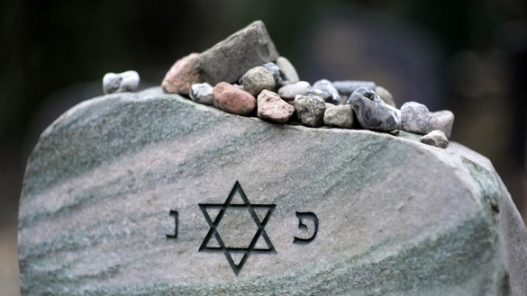 Jüdischer Grabstein mit Davidstern, auf dem viele kleine Steinchen liegen.
