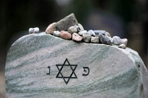 Jüdischer Grabstein mit Davidstern, auf dem viele kleine Steinchen liegen.