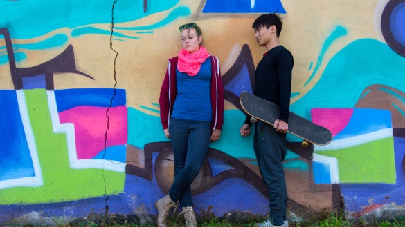 Mädchen und Junge mit Skateboard vor einer Wand mit bunten Graffiti.