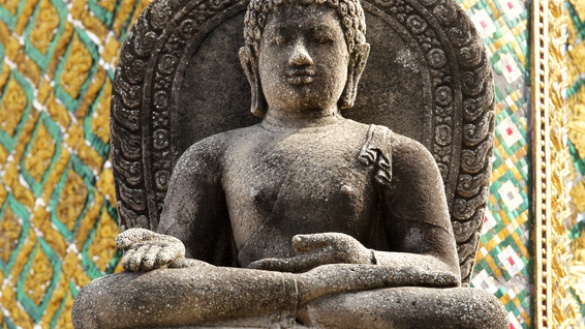 Buddha aus dunkelgrauem Stein mit offener rechter Hand auf dem Knie.