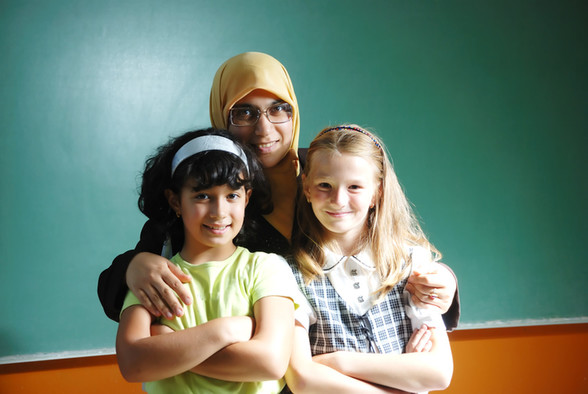 Eine Muslima mit Kopftuch hat ein dunkelhaariges und ein blondes Mädchen im Arm.