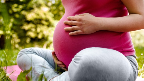 Eine schwangere Frau mit einem roten T-Shirt umfasst mit beiden Händen ihren Bauch.