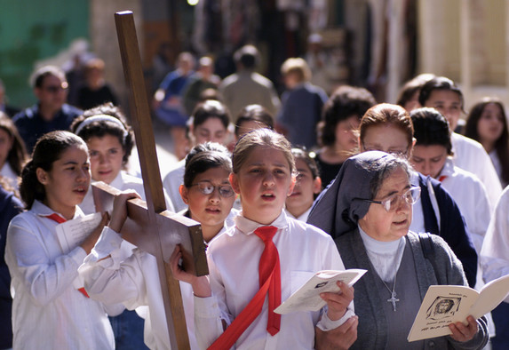 Palästinensische Schülerinnen aus Ost-Jerusalem, die mit ihrer Klasse ein großes Holzkreuz tragen, den Kreuzweg Jesu gehen und beten.