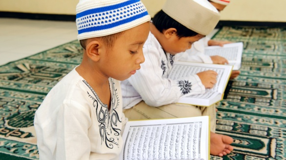 Muslimische Jungen mit Kopfbedeckung lesen im Koran.