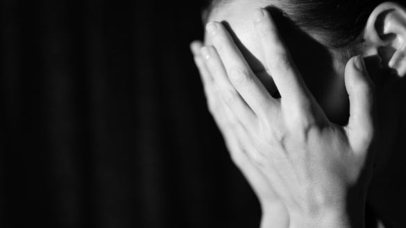 Bild in schwarz-weiß von einer verzweifelten jungen Person, die sich beide Hände vor ihr Gesicht hält.