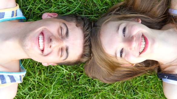Junger Mann und junge Frau liegen Kopf an Kopf auf einer Wiese.