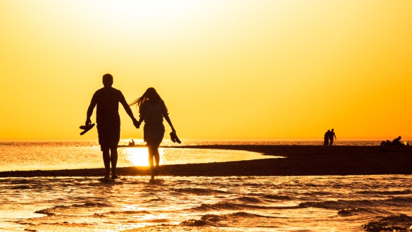 Silhouette eines Paares, das sich an den Händen hält und im Sonnenuntergang am Strand entlang läuft.