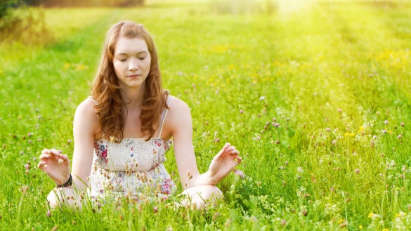 Eine junge Frau sitzt auf einer Wiese und meditiert.
