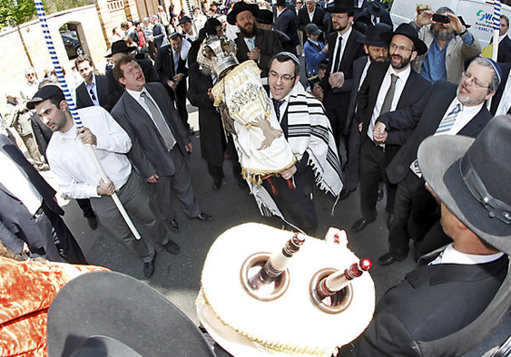 Unter einem schwarzen Baldachin und tanzend und singend tragen Geistliche und männliche Mitglieder der jüdischen Gemeinde Halle eine neue Tora in die Synagoge.
