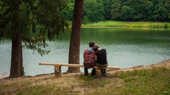 Ein junges Paar sitzt auf einer Bank und blickt auf einen See.